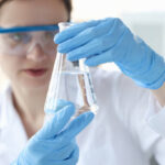 Woman scientist holding flask with transparent liquid in her hands closeup. Checking water quality and ph concept